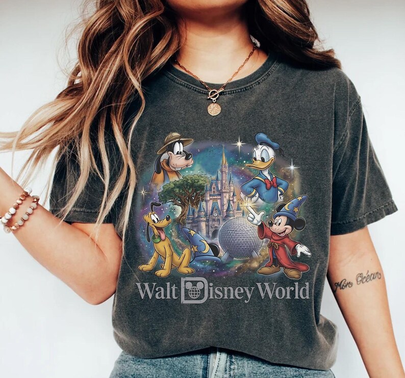 Op de afbeelding: Donkergrijs T-shirt met een kleurrijke afbeelding van Disney-personages, waaronder Mickey Mouse, Donald Duck en Pluto. Het ontwerp bevat een kasteel, een bol en de tekst "Walt Disney World".