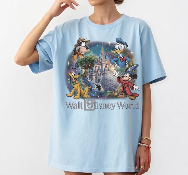 Op de afbeelding: Lichtblauw T-shirt met een kleurrijke afbeelding van Disney-personages, waaronder Mickey Mouse, Donald Duck, Pluto en Goofy. De tekst "Walt Disney World" is ook aanwezig.