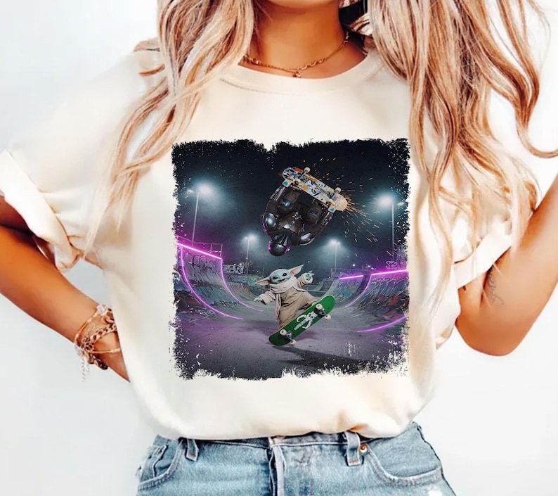 K&ouml;nnte beinhalten: Cremefarbenes T-Shirt mit einer Grafik von Baby Yoda beim Skateboarden in einem Skatepark. Das Design umfasst einen dunklen Hintergrund mit lila Neonlichtern und einen Skateboarder in der Luft.