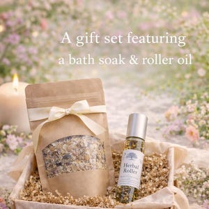 May include: A gift set featuring a bath soak and roller oil. The set includes a brown paper bag with a clear window, a roller bottle, and a gift box, all tied with cream-colored ribbons. The background is a soft, floral arrangement.
