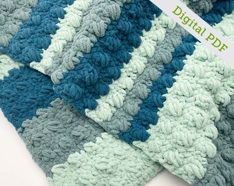 Può includere: Una coperta all'uncinetto in tonalità di blu-verde, blu e verde. La coperta è realizzata con un punto testurizzato che crea un effetto soffice e simile a una nuvola. La coperta è piegata a metà, con un angolo della coperta piegato sull'altro. Il testo "Digital PDF" è visibile nell'angolo in alto a destra dell'immagine.