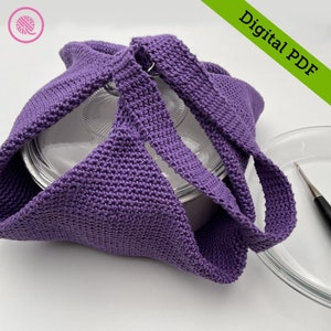 Könnte beinhalten: Eine gehäkelte lila Tragetasche mit zwei Griffen, die einen Glasbehälter hält. Die Tasche ist aus strukturiertem Garn gefertigt und hat ein schlichtes Design. Die Worte "Digital PDF" stehen oben rechts.