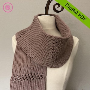 Puede incluir: Una bufanda de punto malva con un delicado patrón de puntadas. La bufanda se muestra en un maniquí blanco.