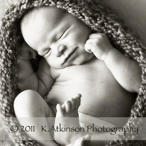 Puede incluir: Un bebé recién nacido duerme plácidamente en una manta de punto. El bebé lleva un pañal blanco y tiene una expresión de paz en su rostro.