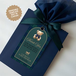 May include: A navy blue gift bag tied with a dark green ribbon and a tag. The tag features a teddy bear illustration and the words "Thank You" and "Baby Shower". The tag has a green and blue plaid pattern. The text "Printable Template Edit in Canva!" is also visible.