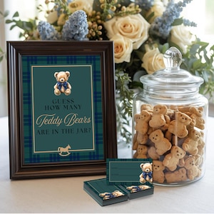 May include: A framed sign with the text "Guess How Many Teddy Bears Are In The Jar?" sits beside a glass jar filled with teddy bear-shaped biscuits. Small cards with teddy bear graphics are stacked nearby. The sign and cards have a green and blue plaid design.