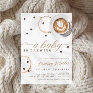 May include: Baby shower invitation with a coffee theme. The invitation features the text "a baby is brewing" in elegant script, coffee bean illustrations, and a cup of latte art. Details include the honoree's name, date, time, and location.