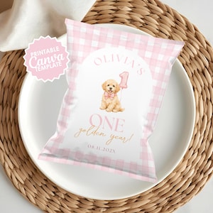 May include: A pink and white gingham-patterned party favor bag with the text "Olivia's 1 One golden year!" and a watercolor illustration of a golden retriever puppy holding a pink balloon. A pink and white "Printable Canva Template" sticker is in the upper left.