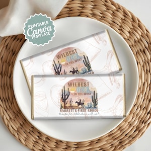 May include: Two chocolate bar wrappers with a Western theme. Each wrapper features a watercolor design with cacti, a cowboy on a horse, and the text "Wildest One in the West." The bottom wrapper reads "Barrett's First Rodeo."