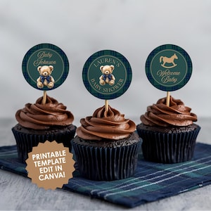 May include: Three cupcakes with chocolate frosting and decorative toppers. The toppers are dark green with a plaid pattern and feature a teddy bear, text that says "Baby Johnson", "Lauren's Baby Shower", and a rocking horse with "Welcome Baby".