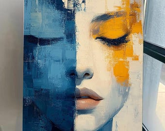 Op de afbeelding: Abstract olieverfschilderij op canvas dat het gezicht van een vrouw afbeeldt, verticaal verdeeld. De ene kant is blauw, de andere wit met gele accenten. De ogen van de vrouw zijn gesloten en haar lippen zijn zachtroze. Het kunstwerk wordt op een houten ezel tentoongesteld.