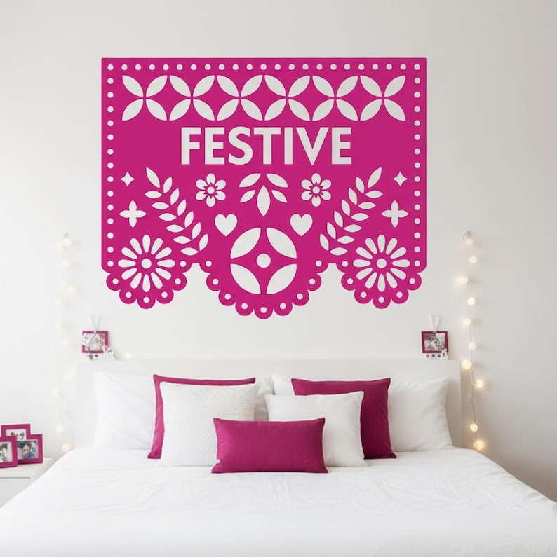 May include: A magenta wall decal with the word "FESTIVE" in white, featuring a decorative design of flowers, leaves, and geometric shapes. The decal is above a bed with white pillows and magenta accent pillows.