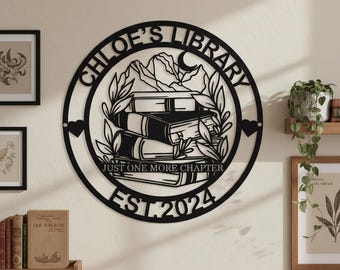 May include: Black metal wall art with the text "CHLOE'S LIBRARY" in a circular design. The art features a stack of books, mountains, and the phrase "JUST ONE MORE CHAPTER" and the year "EST.2024". Two small hearts are on either side.