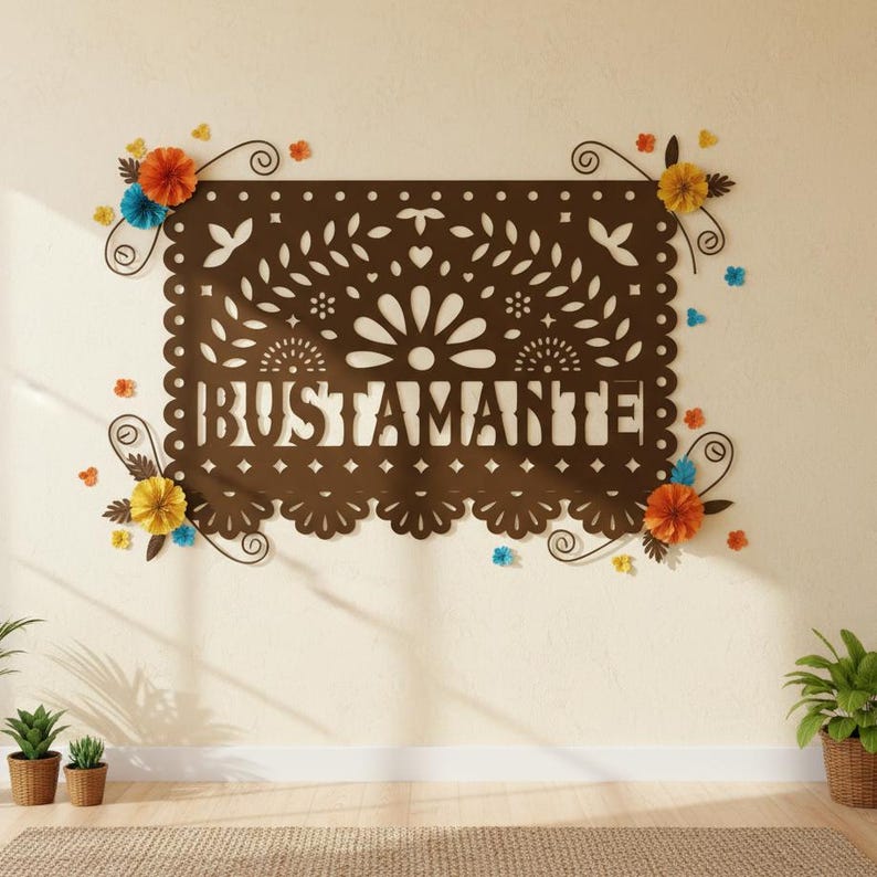 May include: A brown paper-cut wall hanging with the name "BUSTAMANTE" in the center. The design includes floral and leaf patterns, with colorful paper flowers in orange, yellow, and blue accents. The wall is painted a light beige color.