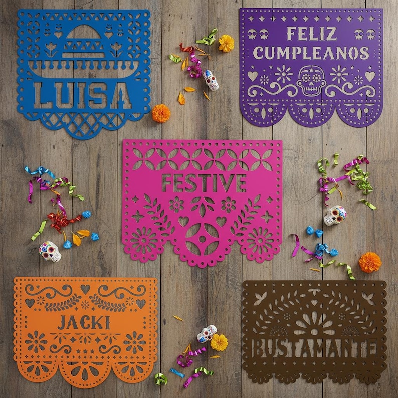 May include: A collection of colorful papel picado banners with intricate cut-out designs. The banners are in blue, purple, pink, orange, and brown, with names and festive phrases. Decorative skulls and colorful confetti are scattered around the banners.