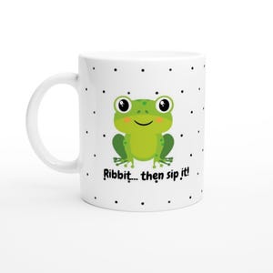 May include: White ceramic mug featuring a green cartoon frog and the text "Ribbit... then sip it!". The mug has a black polka dot pattern and a white handle. A fun and whimsical design.