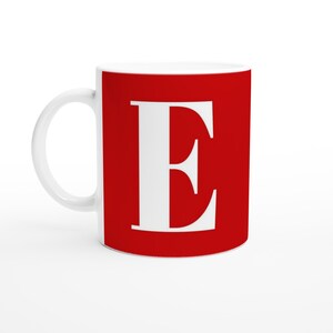 May include: White ceramic mug featuring a large white letter "E" against a red background. The mug has a curved handle and a glossy finish. Suitable for hot or cold drinks. The mug is approximately 9.5 cm tall.