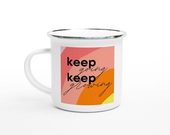 May include: White enamel mug with a silver rim and handle. The mug features a colorful design with the words "keep going, keep growing" in black script. The background has a gradient of pink, orange, and yellow.