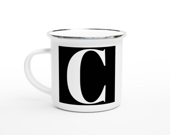 May include: White enamel mug with a black square featuring a large white letter "C". The mug has a silver rim and a white handle. The mug is set against a white background.