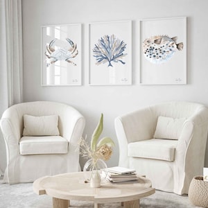 May include: Three framed watercolour prints of sea life, including a crab, coral, and a pufferfish. The prints are hung on a white wall above two white armchairs and a wooden coffee table.