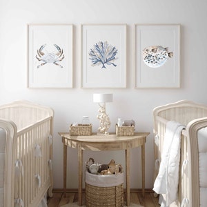 May include: A nursery room with two cots, a wooden side table with a lamp, and three framed watercolour prints of a crab, coral, and a pufferfish. The table has a wicker basket with the word "Toys" on it.