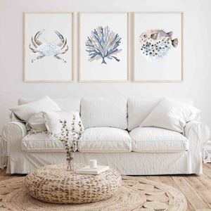 May include: Three framed watercolour prints of sea life, including a crab, coral, and a pufferfish. The prints are displayed on a white wall above a white sofa.