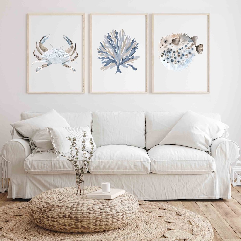May include: Three framed watercolour prints of sea life, including a crab, coral, and a pufferfish. The prints are displayed on a white wall above a white sofa.