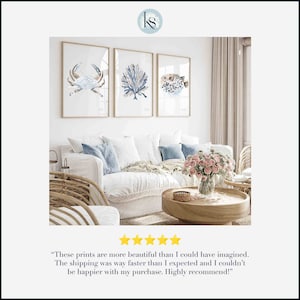 May include: Three framed watercolour prints of a crab, coral, and a pufferfish in blue and brown tones. The prints are hanging on a white wall above a white sofa with blue cushions.