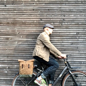 May include: A person riding a black electric bicycle with a brown canvas pannier bag attached to the rear rack. The bicycle has a black frame, black wheels, and a black seat.