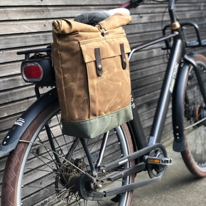 May include: A brown canvas bike bag with leather straps and a green trim is attached to the rear rack of a black electric bicycle.