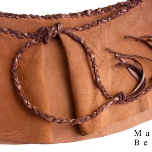 May include: A brown leather belt with a braided design and fringe tassels. The belt is tied in a knot at the front. The text "Mano Bello" is printed on the bottom right corner of the image.