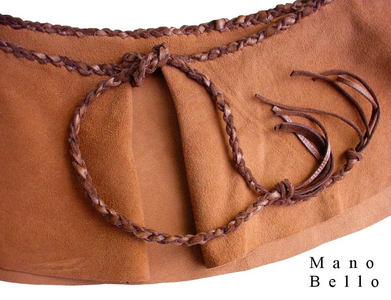 May include: A brown leather belt with a braided design and fringe tassels. The belt is tied in a knot at the front. The text "Mano Bello" is printed on the bottom right corner of the image.