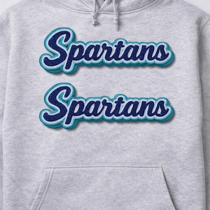 Puede incluir: Sudadera con capucha gris claro con bolsillo delantero y capucha con cordón. La palabra "Spartans" está bordada en azul y turquesa en el pecho, con un efecto de sombra para mayor dimensión. Una prenda casual y cómoda.