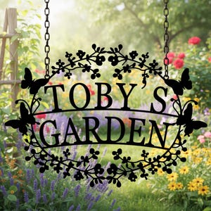 May include: Black metal garden sign with the text "TOBY'S GARDEN". The sign is oval-shaped, adorned with floral and butterfly cutouts, and suspended by chains. The background features a vibrant garden with colorful flowers.