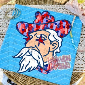 May include: A light blue t-shirt featuring a graphic of a person with a white beard and hair wearing a red, white, and blue patterned cowboy hat. The person has red star-shaped glasses over their eyes. The text LOKK VIEW DESIGNS is visible.