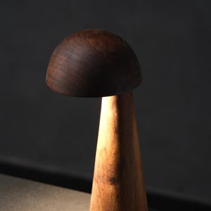 Puede incluir: Lámpara de madera con forma de hongo, con una tapa marrón oscuro y una base cónica marrón claro. La lámpara se ilumina desde dentro, proyectando un brillo cálido. Diseño minimalista y moderno, adecuado para la decoración del hogar.