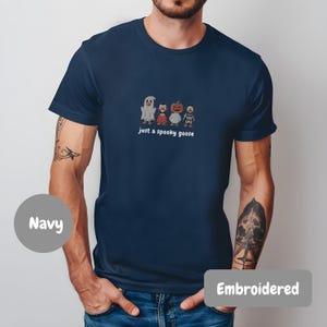 A man wearing a navy blue t-shirt with a graphic of four cartoon characters and the text "Just a spooky goose" printed on it.