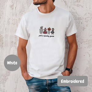 A man wearing a white t-shirt with a graphic of four cartoon characters and the text "Just a spooky goose" printed on it.