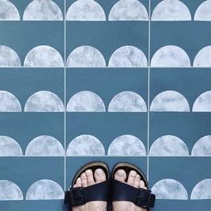May include: A close-up of a blue tiled floor with white half-circle designs. Two brown sandals with white soles are on the floor.