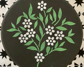 Könnte beinhalten: Eine schwarze runde Oberfläche mit einem weißen Blumenmuster, das darauf gemalt ist. Die Blumen sind weiß mit grünen Blättern und Stielen.