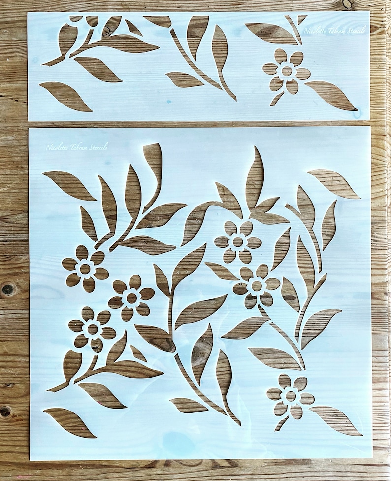 K&ouml;nnte beinhalten: Zwei wei&szlig;e Kunststoff-Schablonen mit einem floralen Design. Die obere Schablone hat eine einzelne Reihe von Blumen und Bl&auml;ttern. Die untere Schablone hat ein aufwendigeres Design mit mehreren Blumen und Bl&auml;ttern.