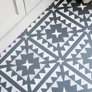 Pode incluir: Um piso cinza com um padrão geométrico branco. O padrão é composto por quadrados, triângulos e estrelas.