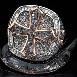 May include: A large, ornate ring with a cross design. The ring features a silver band with a rose gold cross set with numerous small diamonds. The cross has the numbers 0, 3, 6, and 9. The ring is set with many small diamonds.