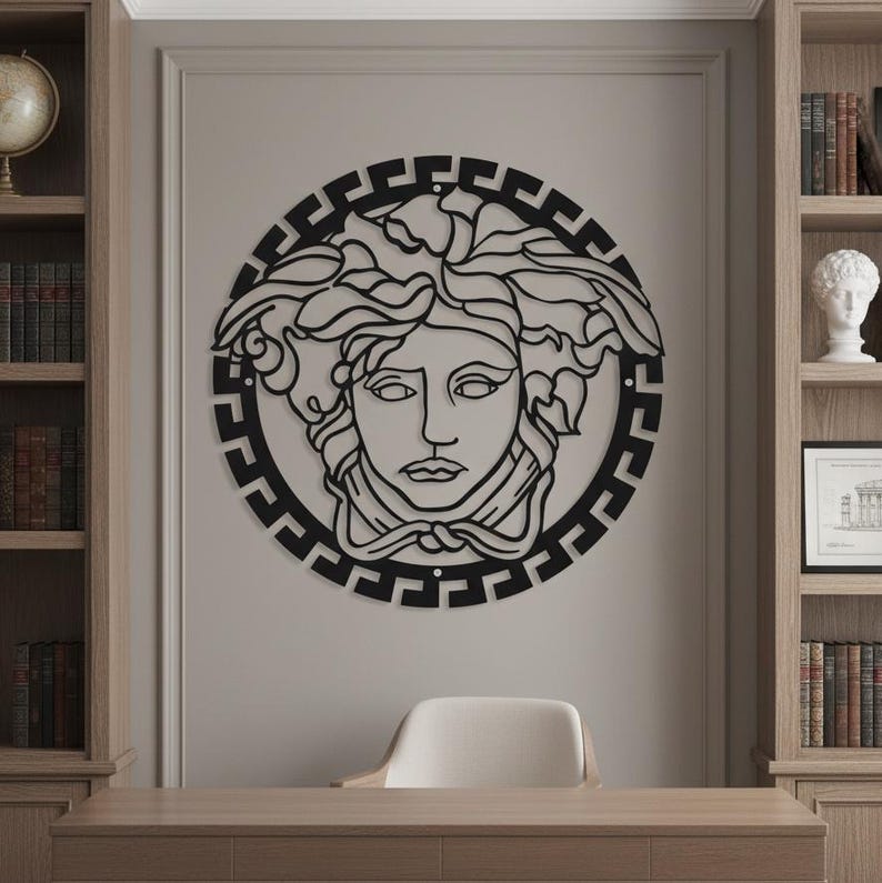 May include: Black metal wall art featuring the iconic Medusa head design within a circular frame. The artwork is mounted on a neutral-colored wall, with a desk and chair in the foreground. The design is a classic symbol of luxury and fashion.