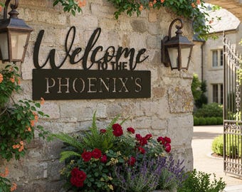 Peut inclure: Un panneau en métal noir avec l'inscription "Welcome to the Phoenix's" est fixé à un mur en pierre. Le panneau est entouré de plantes grimpantes, de lanternes et d'une jardinière en pierre remplie de roses rouges et de lavande.