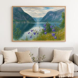 May include: A framed landscape painting depicts a serene lake scene with mountains in the background. The artwork features a reflective lake, lush greenery, and vibrant purple wildflowers in the foreground. The painting is displayed above a gray sofa.