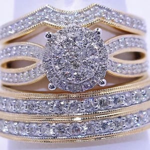 Könnte beinhalten: Ein dreiteiliges Brautring-Set. Die Ringe haben goldene Bänder mit Reihen aus kleinen, klaren Steinen. Der zentrale Ring hat einen großen, runden Cluster aus klaren Steinen. Das Set enthält ein passendes Band und ein gebogenes Band.