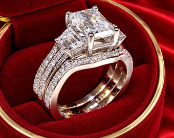 May include: A silver-toned engagement ring set featuring a large rectangular radiant-cut center stone flanked by two smaller rectangular side stones, with pavé-set diamonds along the bands and a matching curved wedding band.