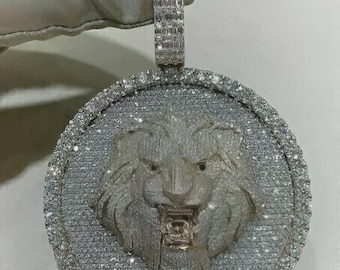 May include: A silver pendant featuring a detailed lion's head with an open mouth, set within a circular frame. The pendant is encrusted with numerous small, sparkling stones, and has a rectangular bail for a chain.