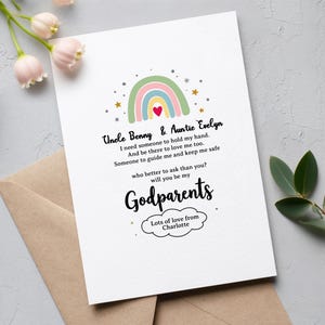 Puede incluir: Una tarjeta blanca con un diseño de arcoíris colorido y el texto "Uncle Benny & Auntie Evelyn, will you be my Godparents?" La tarjeta está sobre un sobre marrón claro, con un arreglo floral en el fondo.